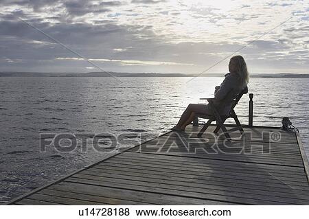 Stock Photo - Young Woman relaxing on jetty.. Fotosearch