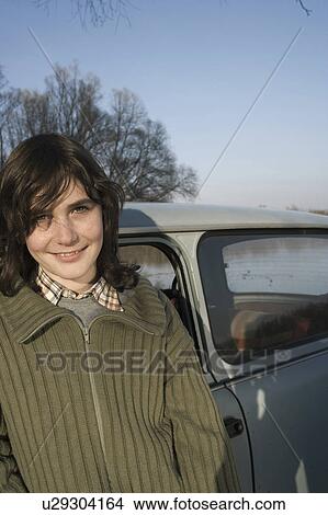 Picture - Boy (12-14) standing by car, smiling, portrait. Fotosearch