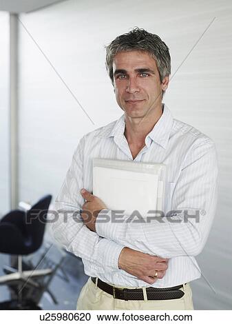 Businessman standing in office holding file, portrait View Large Photo Image Stock Image - Businessman standing in office holding file, portrait. Fotosearch
