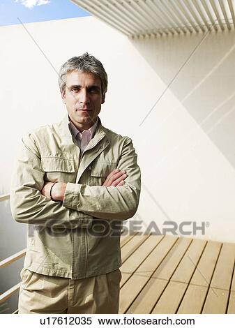 Stock Photography - Man standing on balcony, arms crossed, portrait. Fotosearch