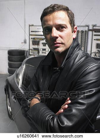 Stock Image - Portrait of a man leaning on a Porsche in a garage.. Fotosearch