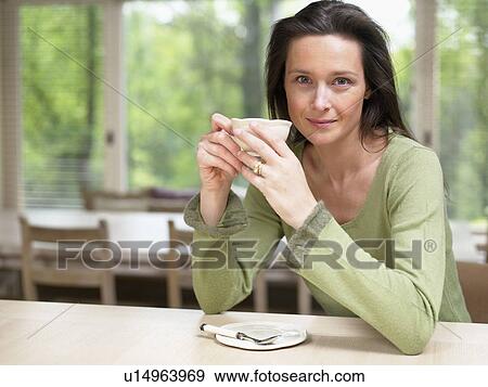 Woman holding a mug at a table indoors smiling. View Large Photo Image Stock Photo - Woman holding a mug at a table indoors smiling.. Fotosearch