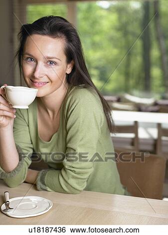 Woman holding a mug at a table indoors smiling. View Large Photo Image Stock Photograph - Woman holding a mug at a table indoors smiling.. Fotosearch