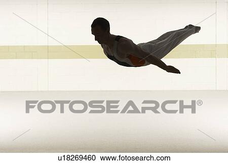 Stock Image - Male gymnast performing somersault in floor exercise. Fotosearch