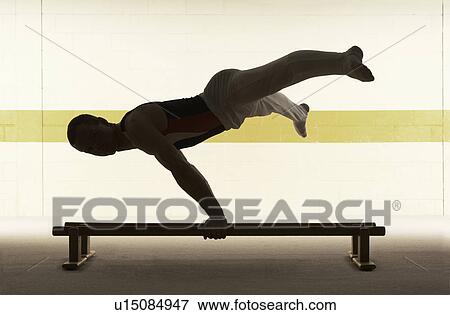 Male Gymnast Practising On Floor Bar Side View Stock Photo