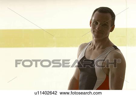 Stock Image - Male gymnast standing in gymnasium, smiling, portrait. Fotosearch