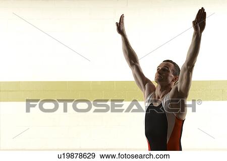 Male gymnast standing with arms raised above head View Large Photo Image Stock Photo - Male gymnast standing with arms raised above head. Fotosearch