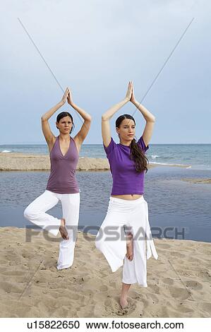 Stock Image - Two women doing yoga on beach.. Fotosearch