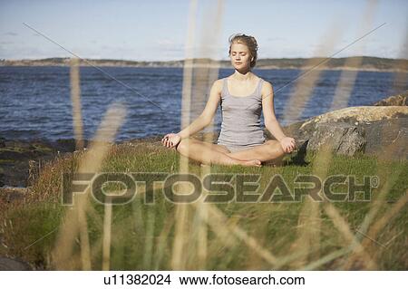 Picture - Young Woman doing Yoga on grass by sea.. Fotosearch