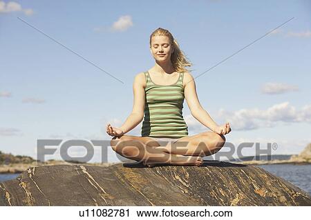 Stock Image - Young Woman doing Yoga on rocks.. Fotosearch