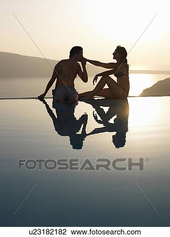 Stock Image - Couple sitting on the edge of pool. Fotosearch