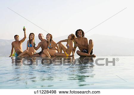 Stock Photo - Men and women sitting by edge of pool. Fotosearch