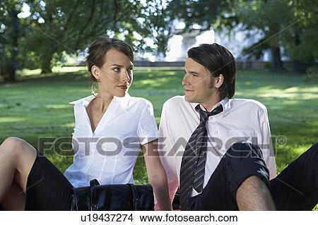 Businessman and woman sitting in meadow in park watching each other. View Large Photo Image Picture - Businessman and woman sitting in meadow in park watching each other.. Fotosearch