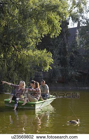 Stock Image - Four friends in a rowboat smiling and pointing.. Fotosearch