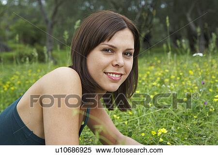 Stock Photography - Portrait of young woman lying in meadow smiling olive trees in background.. Fotosearch