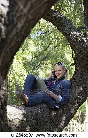 Woman sitting in a tree on cellular phone smiling. View Large Photo Image Stock Photo - Woman sitting in a tree on cellular phone smiling.. Fotosearch