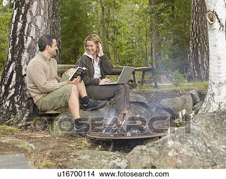 Woman with laptop and man with book near a fire pit smiling. View Large Photo Image Picture - Woman with laptop and man with book near a fire pit smiling.. Fotosearch