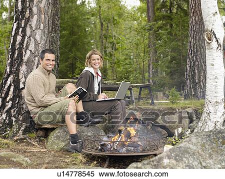 Woman with laptop and man with book near a fire pit smiling. View Large Photo Image Stock Photography - Woman with laptop and man with book near a fire pit smiling.. Fotosearch