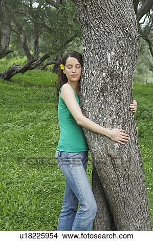 Picture - Young woman hugging tree in orchard with eyes closed.. Fotosearch