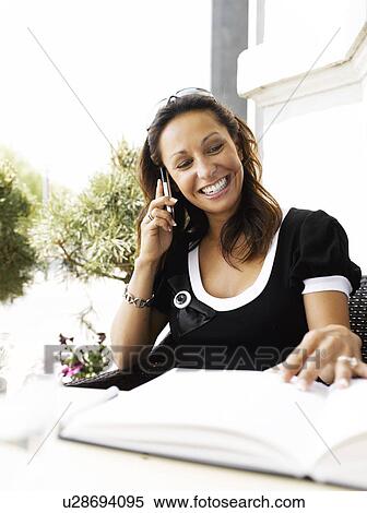 Stock Photography - Woman on her cell phone at an outdoor restaurant. Fotosearch