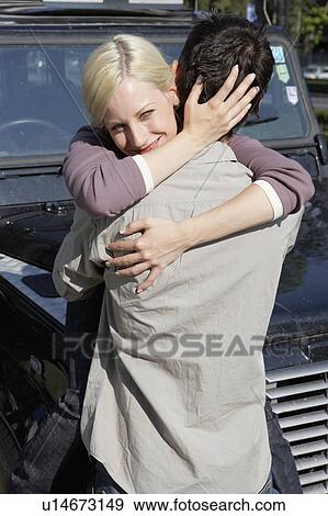 Stock Photo - Couple embracing by an SUV smiling.. Fotosearch