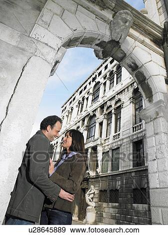 Stock Photo - Couple embracing under stone arch. Venice, Italy.. Fotosearch