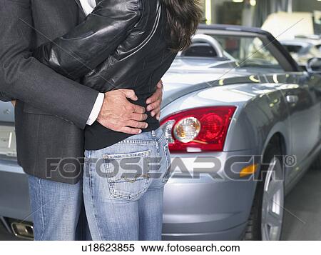 Stock Photography - Couple holding each other in front of a convertible close up.. Fotosearch