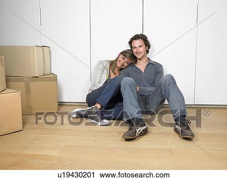 Stock Image - Couple sitting on floor smiling with moving boxes nearby.. Fotosearch