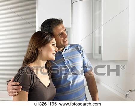 Stock Photography - Couple standing in kitchen, heads together. Fotosearch