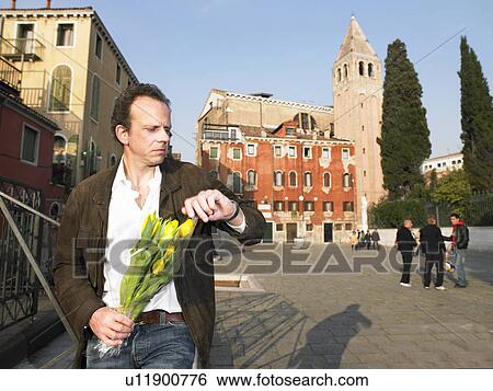 Stock Photograph - Man waiting with bunch of tulips, looking at his watch. Venice, Italy.. Fotosearch