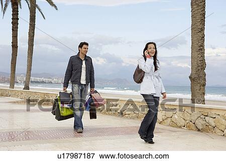 Stock Photo - Woman using mobile phone, man carrying shopping in background. Fotosearch
