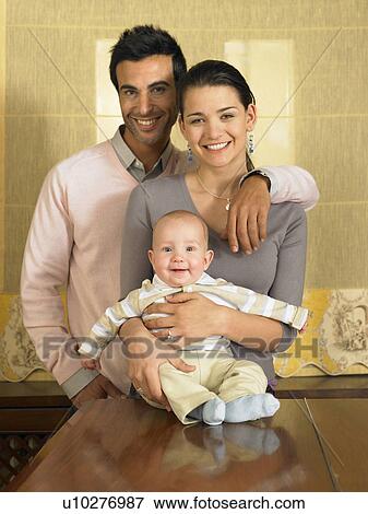Stock Photo - Young couple and baby son (1-3 months) smiling, portrait. Fotosearch