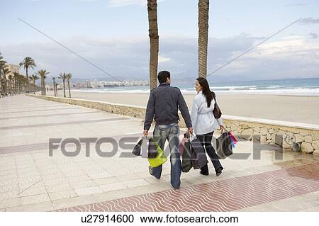 Young couple carrying shopping walking on promenade View Large Photo Image Stock Image - Young couple carrying shopping walking on promenade. Fotosearch