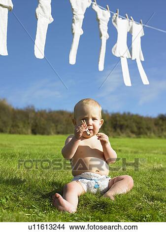 Picture - Baby sitting and holding clothes peg.. Fotosearch