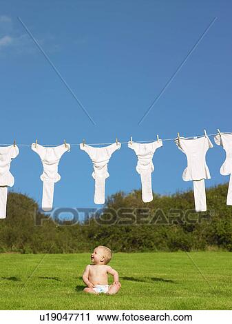 Stock Image - Baby sitting on grass, looking up.. Fotosearch