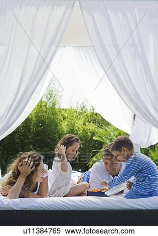 Stock Photography - Family having breakfast on bed in garden. Fotosearch