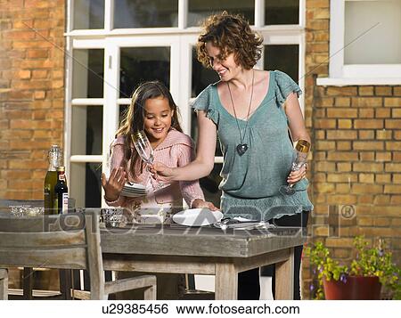 Stock Photograph - Mother and daughter laying table outside. Fotosearch
