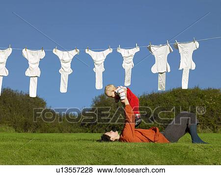 Mother lying on grass holding up baby View Large Photo Image Stock Photo - Mother lying on grass holding up baby. Fotosearch