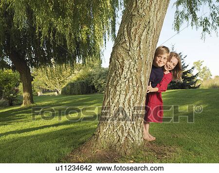 Young boy and girl hiding behind tree View Large Photo Image Stock Image - Young boy and girl hiding behind tree. Fotosearch