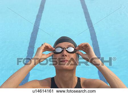 Stock Image - Female swimmer adjusting goggles by pool, close-up. Fotosearch