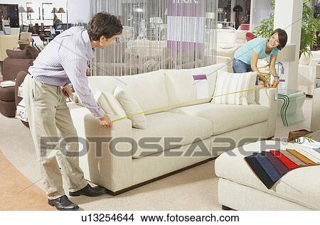 A couple measuring a sofa in a shop. View Large Photo Image Picture - A couple measuring a sofa in a shop.. Fotosearch
