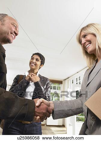 Real estate agent shaking hands with male client beside female client. View Large Photo Image Stock Photo - Real estate agent shaking hands with male client beside female client.. Fotosearch