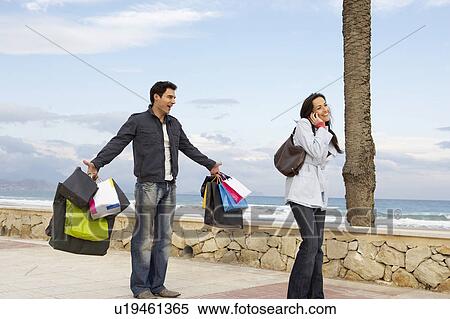 Woman using mobile phone, man holding out shopping bags in background View Large Photo Image Stock Photography - Woman using mobile phone, man holding out shopping bags in background. Fotosearch