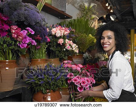 Young female florist holding flowers, smiling, portrait View Large Photo Image Stock Photo - Young female florist holding flowers, smiling, portrait. Fotosearch
