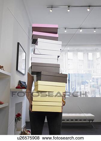 Stock Photo - Young woman holding pile of shoe boxes obscuring face. Fotosearch