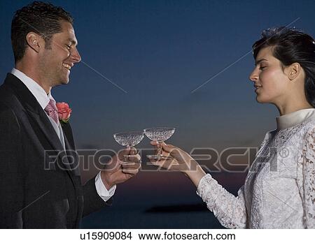Bride and groom toasting each other with champagne, smiling, sunset View Large Photo Image Picture - Bride and groom toasting each other with champagne, smiling, sunset. Fotosearch
