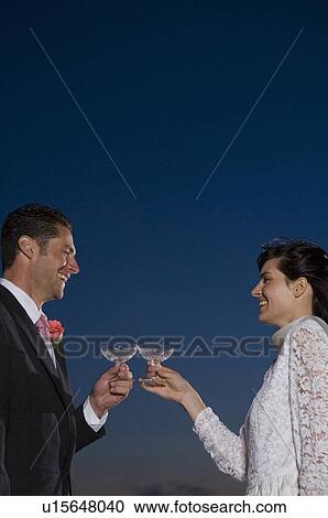 Bride and groom toasting each other with champagne, smiling, sunset View Large Photo Image Stock Image - Bride and groom toasting each other with champagne, smiling, sunset. Fotosearch