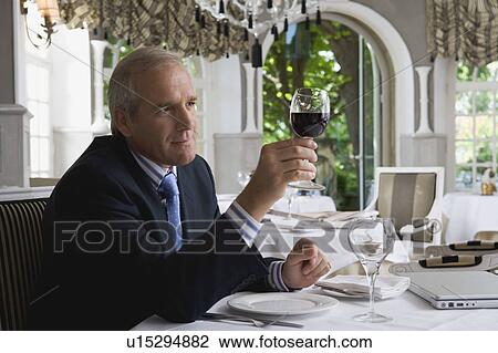 Stock Image - Businessman looking at a glass of wine in a restaurant. Fotosearch