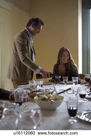 Stock Image - Man pouring wine for woman at dinner table. Fotosearch