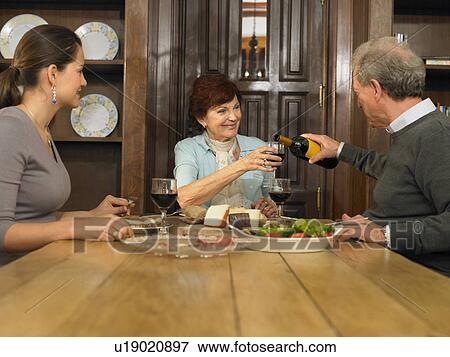 Young woman and senior parents having lunch, man pouring wine View Large Photo Image Stock Photo - Young woman and senior parents having lunch, man pouring wine. Fotosearch
